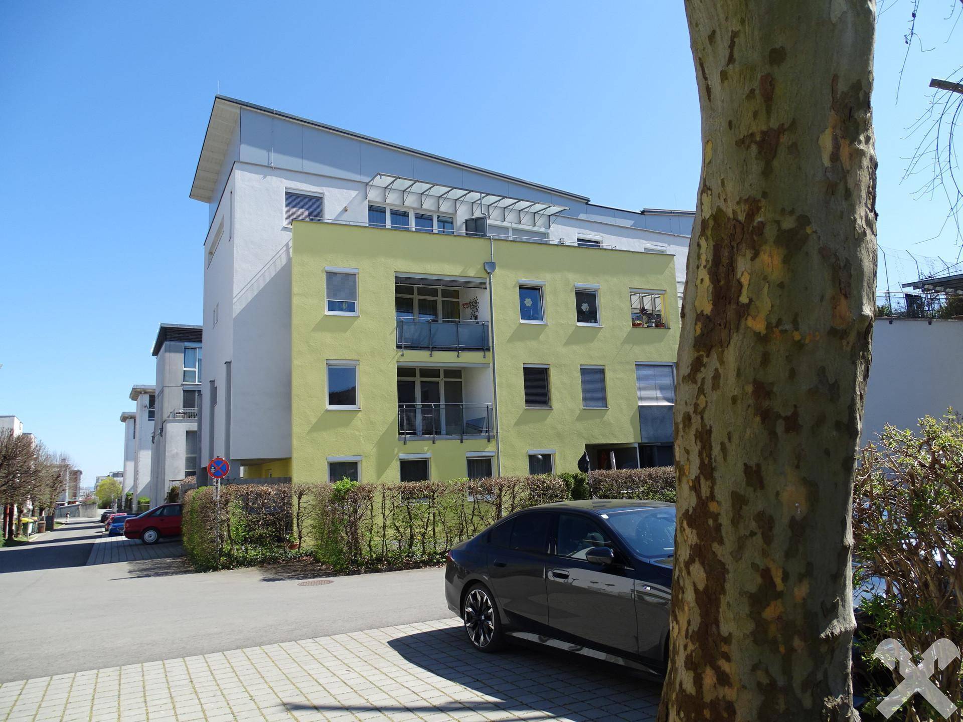 Gesamtansicht der Wohnanlage mit gelber Fassade, umgeben von Bäumen und Parkplätzen.