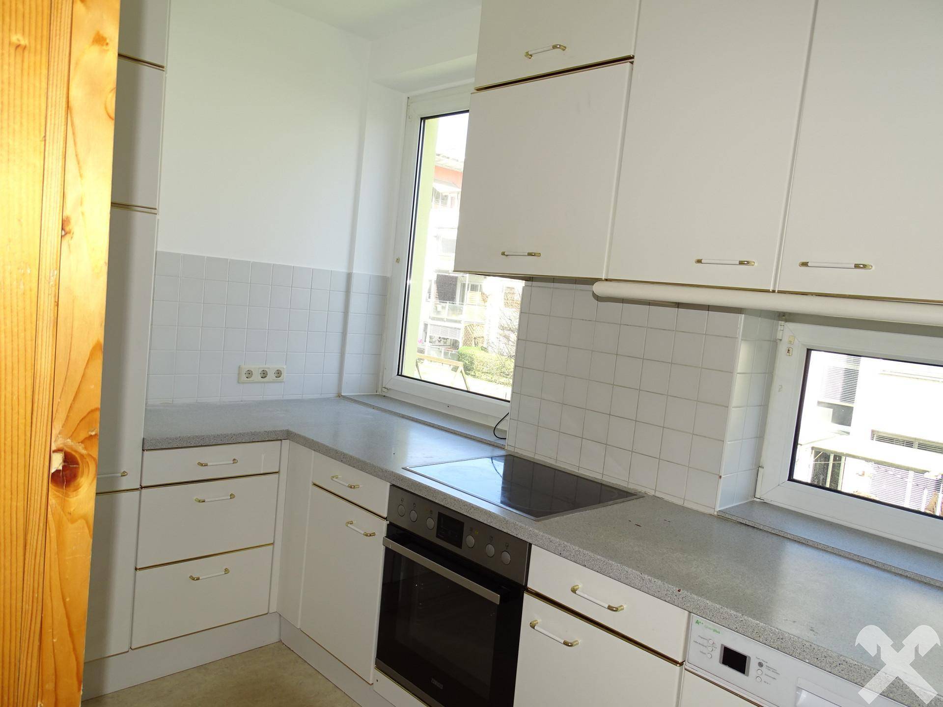 Funktionale Küche mit weißen Schränken, integriertem Backofen und Fenster.