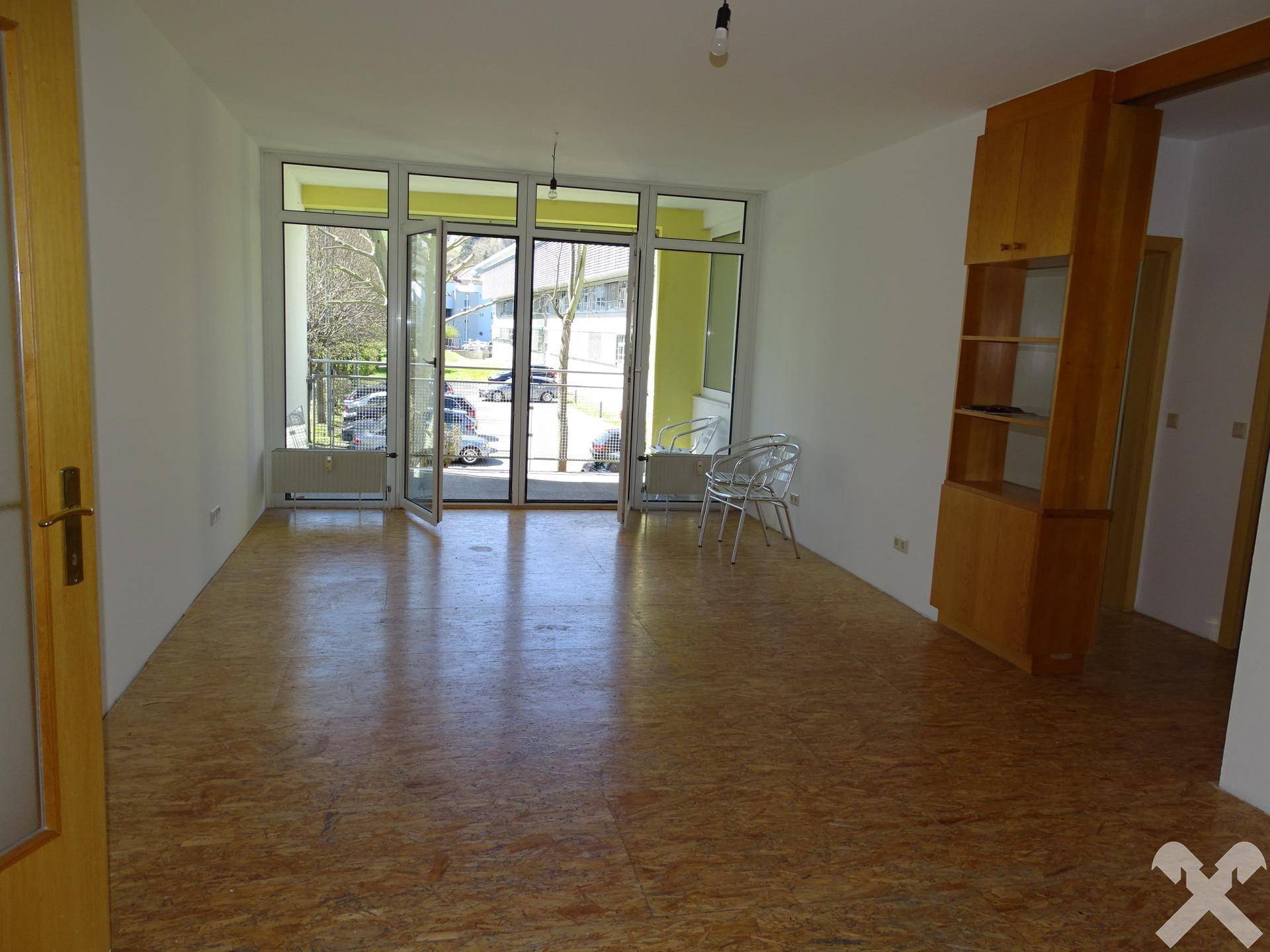 Heller Wohnbereich mit großen Fenstern, Zugang zum Balkon und Laminatboden.