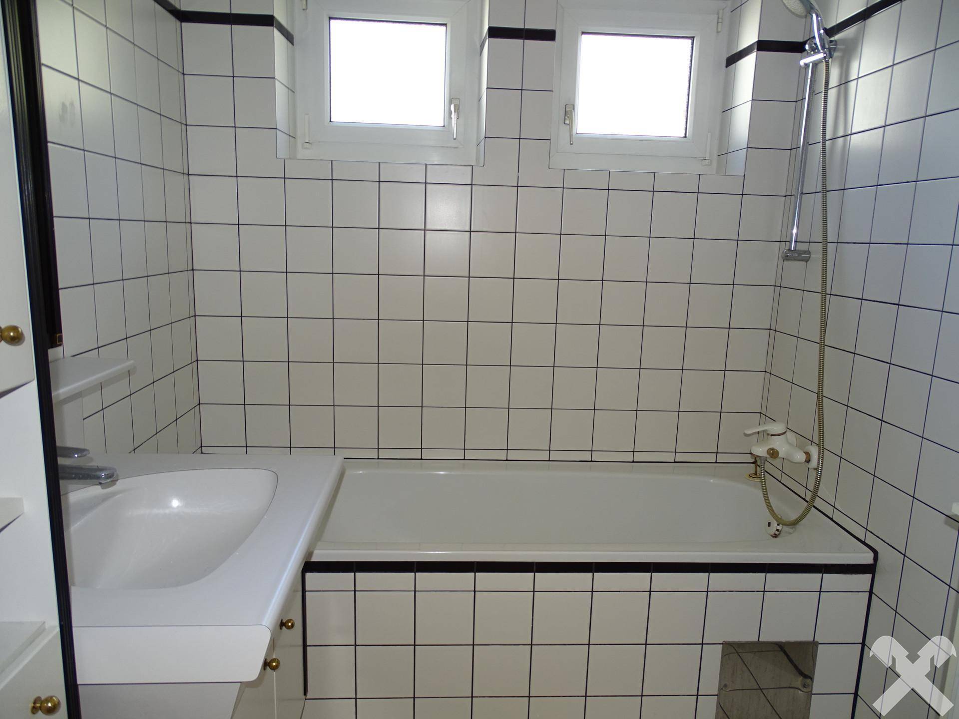 Badezimmer mit Badewanne, Duschfunktion und weißen Fliesen mit schwarzen Akzenten.