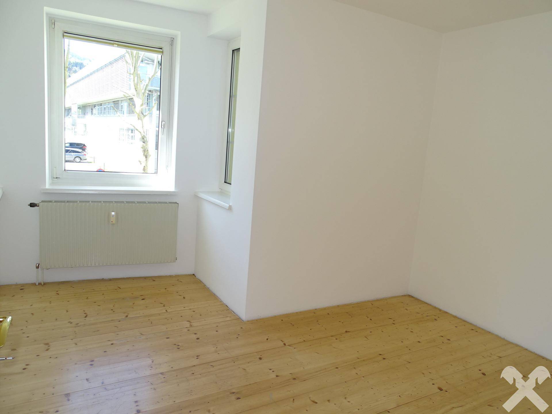 Helles Zimmer mit Holzboden, weißen Wänden und zwei Fenstern für gute Belichtung.