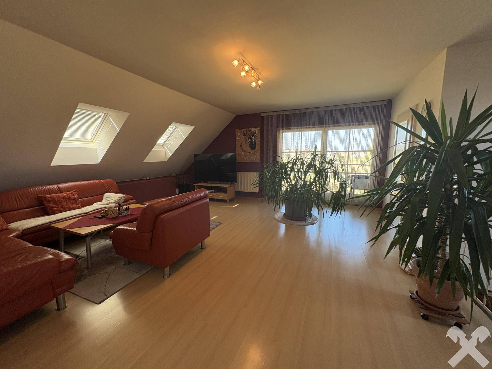 Helles Wohnzimmer im Dachgeschoss mit roten Ledersofas, Holzboden und Dachfenstern.