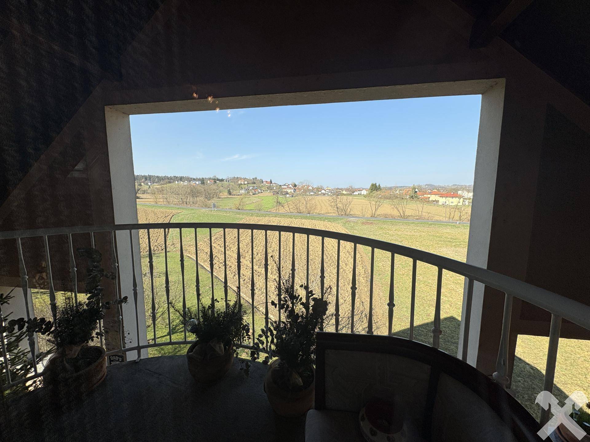 Blick vom Balkon auf die weite, grüne Landschaft und die umliegenden Felder unter blauem Himmel.