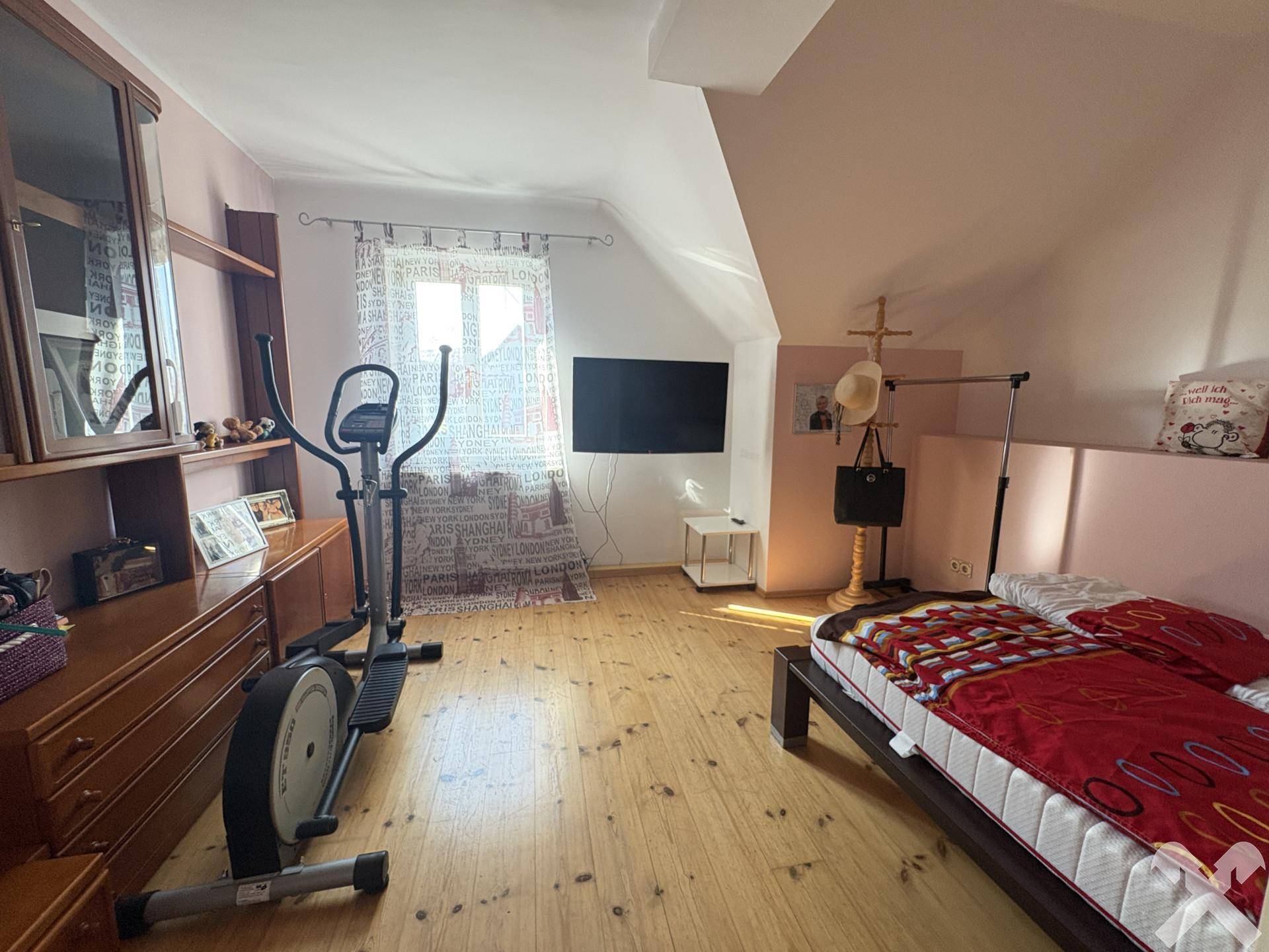 Geräumiges Schlafzimmer mit Holzboden, Trainingsgerät und rosa Akzenten im Dachgeschoss.