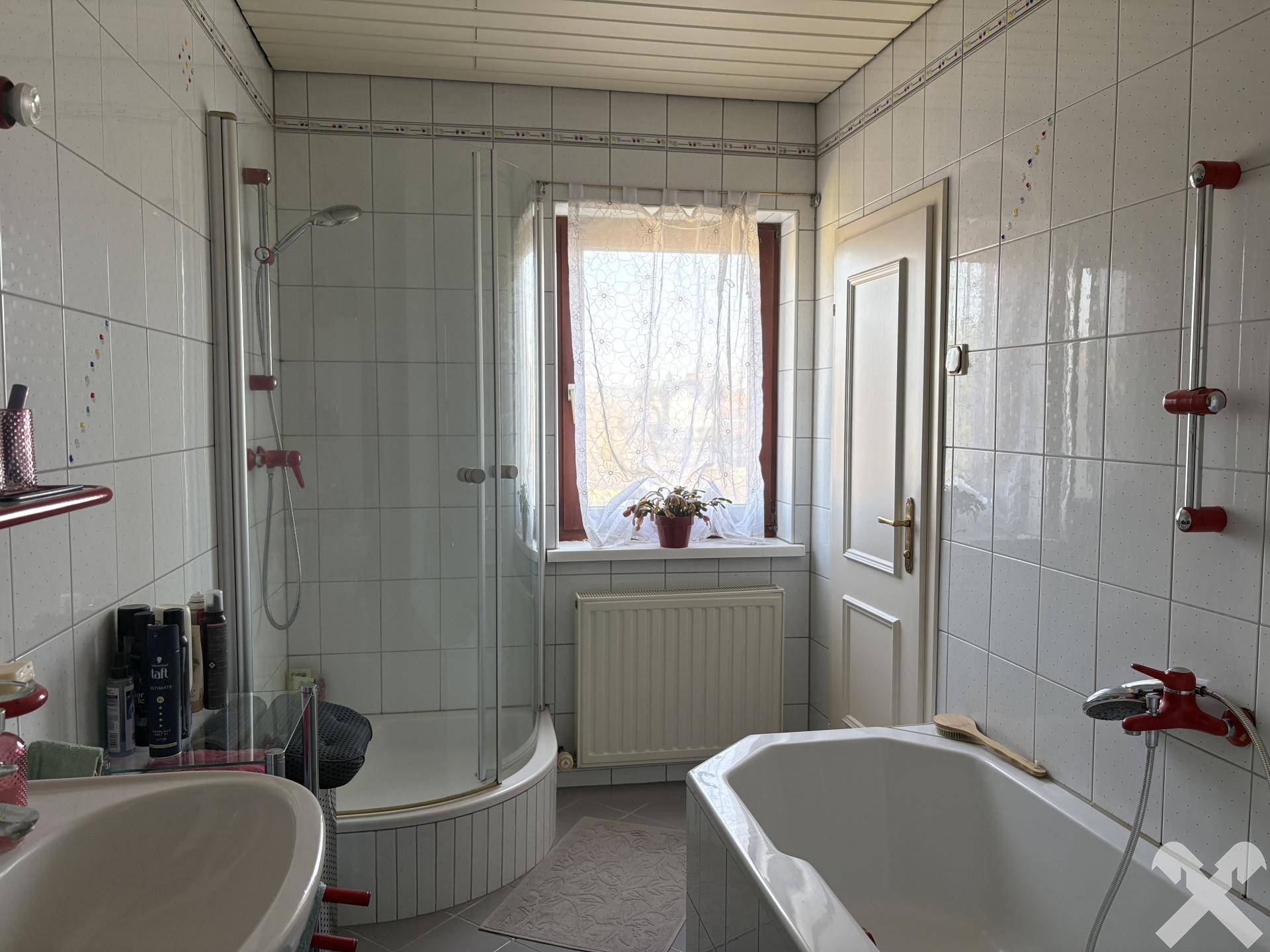 Badezimmer mit weißen Fliesen, Duschkabine, Badewanne und Fenster für Tageslicht.