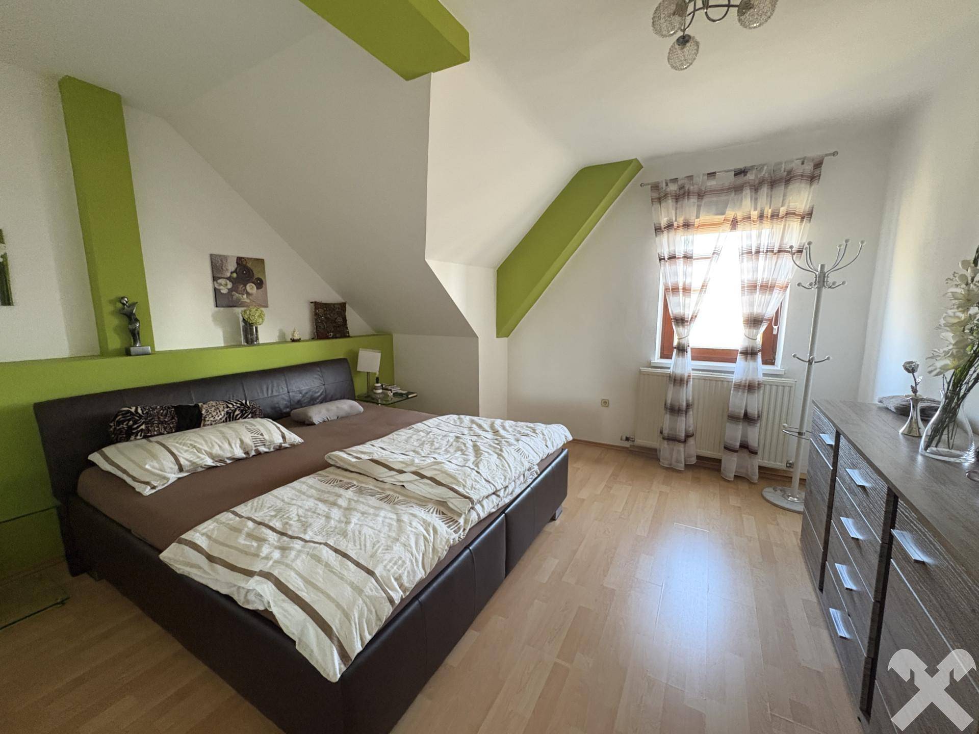 Schlafzimmer im Dachgeschoss mit Doppelbett, Holzboden und grünen Akzentwänden.