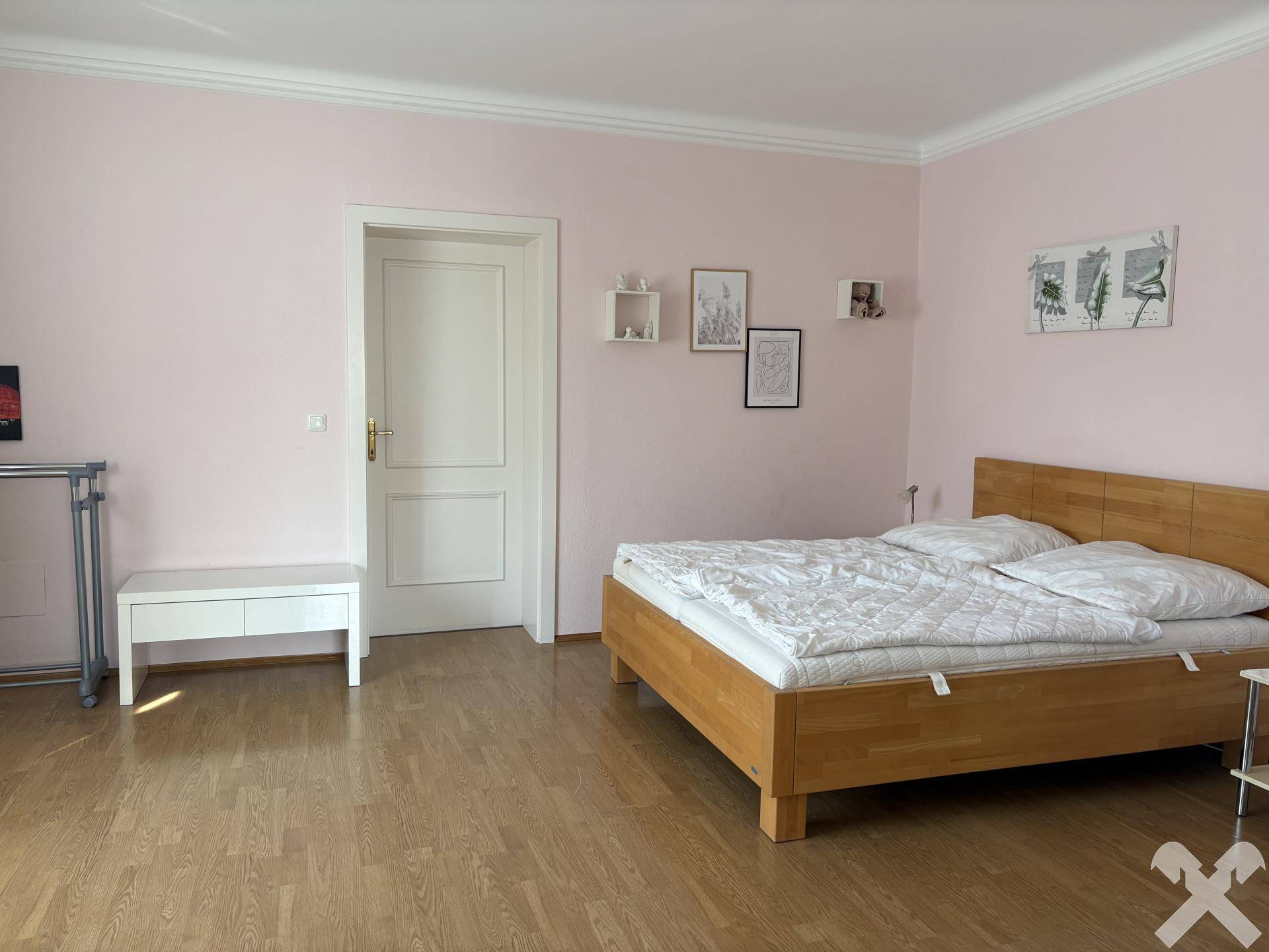 Helles Schlafzimmer mit Doppelbett, Holzboden und zartrosa Wänden.