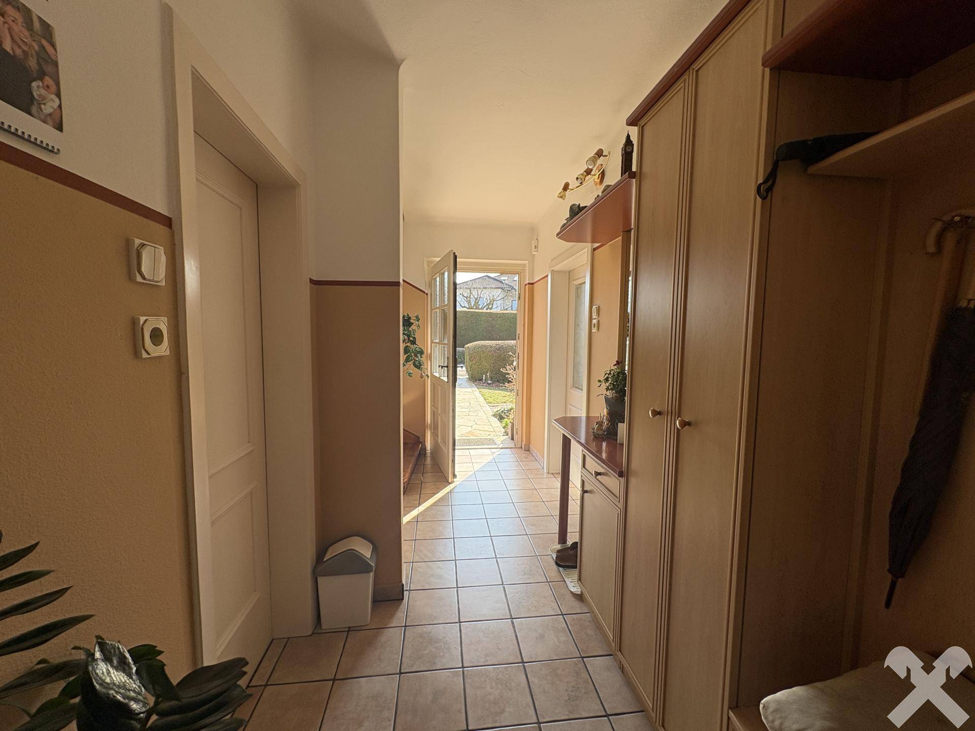 Heller Flur mit Fliesenboden, Garderobe und Blick in den Gartenbereich.