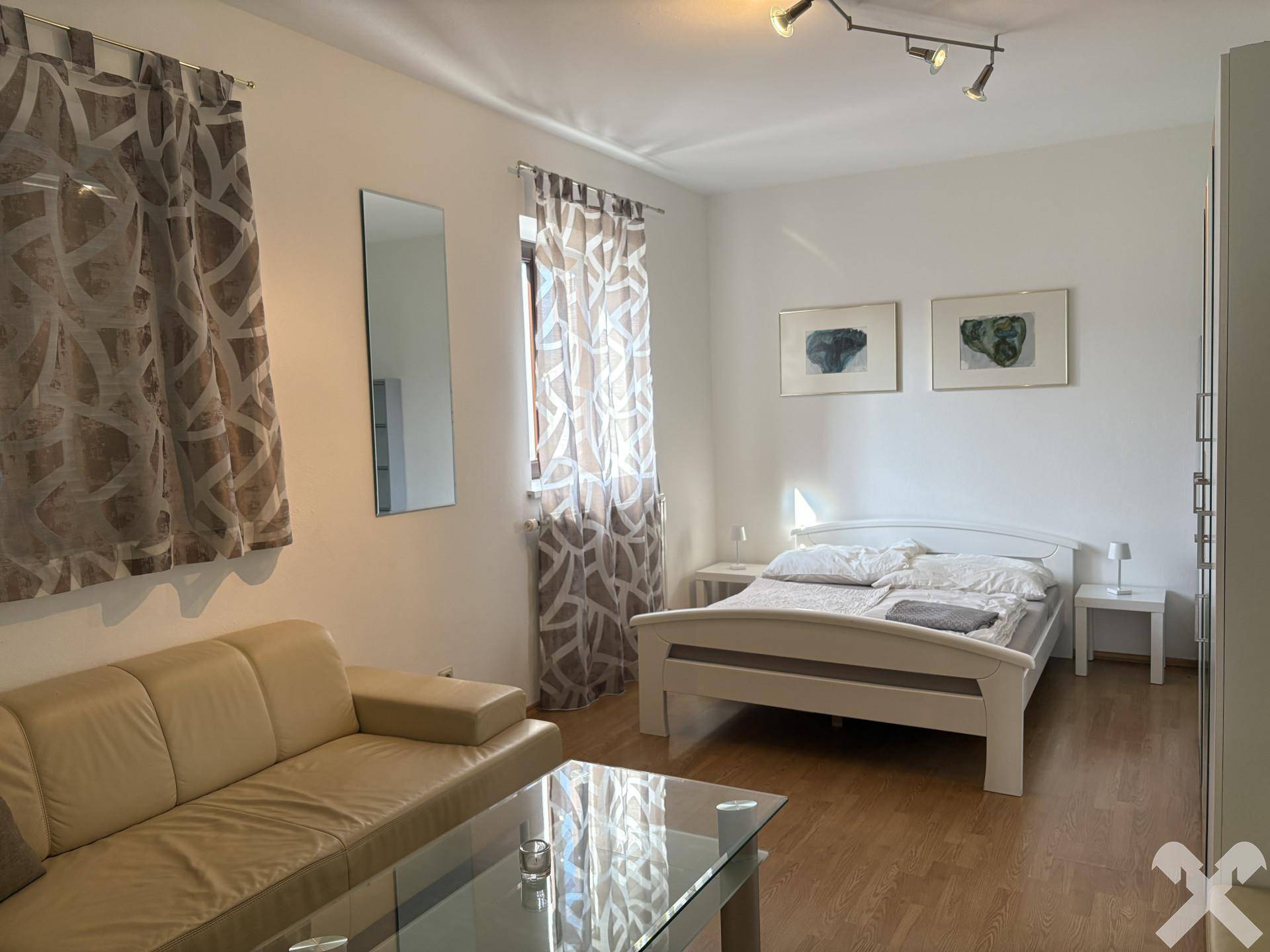 Schlafzimmer mit Doppelbett, Sofa, Couchtisch und Holzboden, hell und freundlich gestaltet.