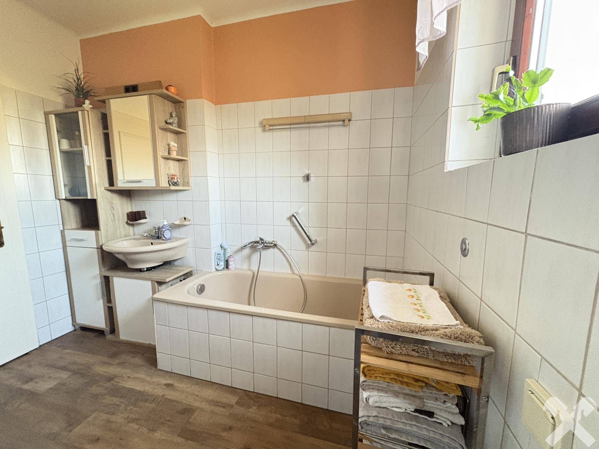 Badezimmer mit Badewanne, Waschbecken, Spiegelschrank und Fenster, in warmen Farbtönen.