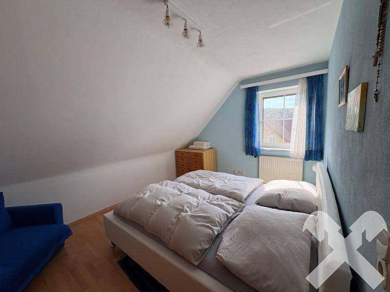 Gemütliches Schlafzimmer im Dachgeschoss mit blauer Wand und Holzboden.