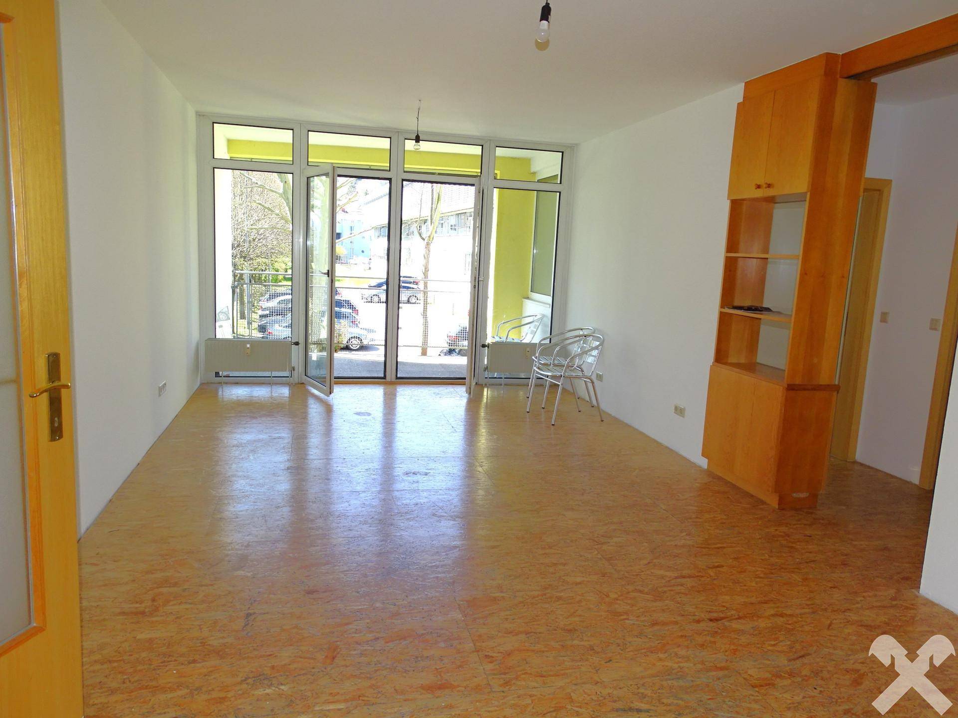Heller Wohnbereich mit großen Fenstern, Zugang zum Balkon und Laminatboden.