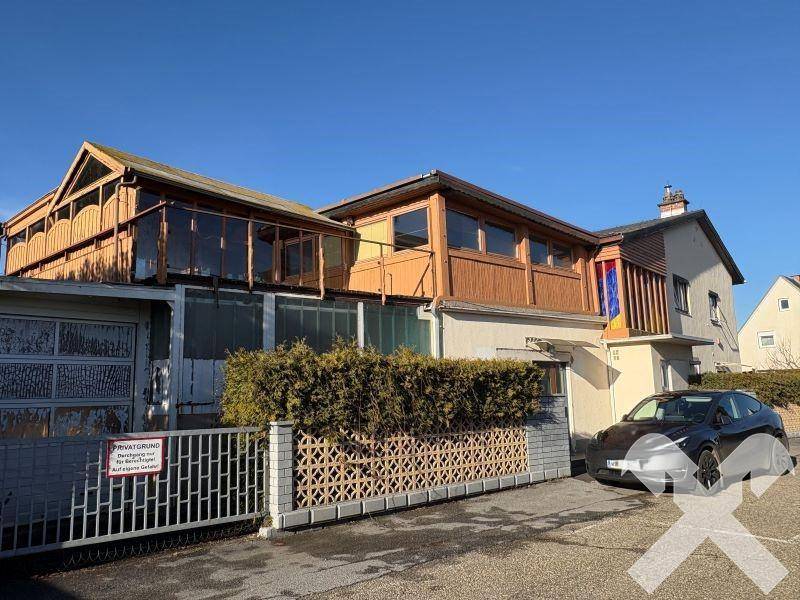 Seitenansicht des Gebäudes mit Garage, Holzbalkonen und einem geparkten Auto.