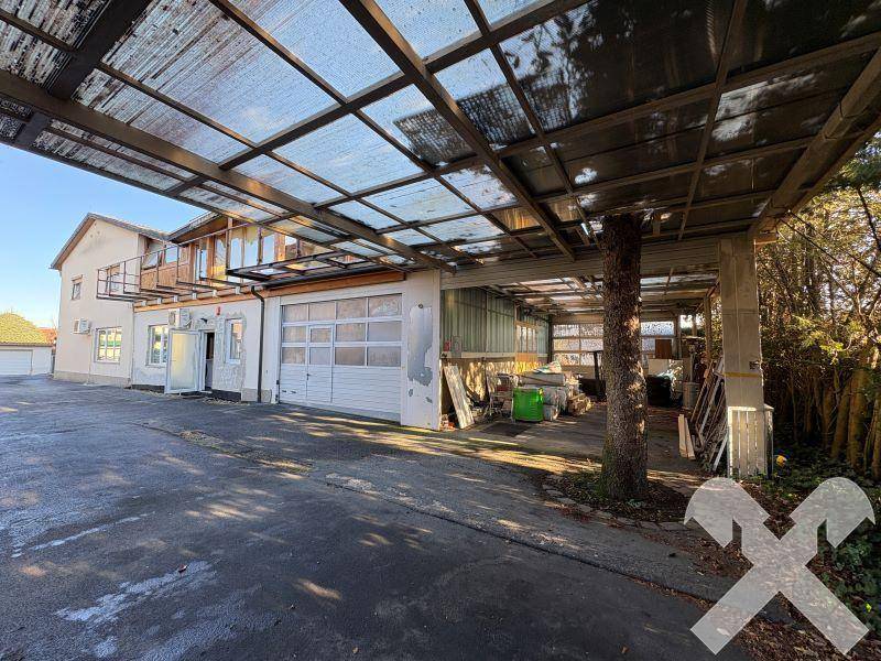 Großer überdachter Bereich neben dem Gebäude mit Garagentoren und viel Platz.