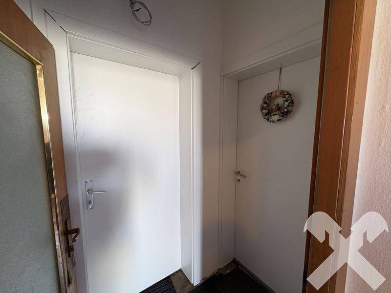 Einfacher Flur mit zwei weißen Türen und einem dekorativen Kranz an der Wand.
