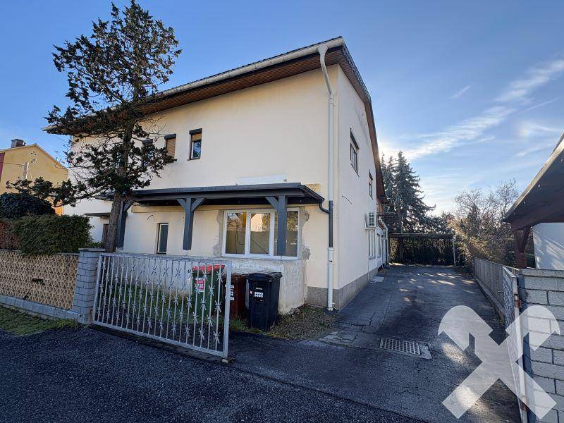 Rückansicht des Gebäudes mit Einfahrt, Mülltonnen und einem stabilen Zaun.