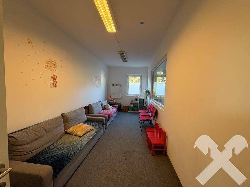 Langer Raum mit bequemen Sofas, Teppichboden und kleinen Fenstern für natürliches Licht.