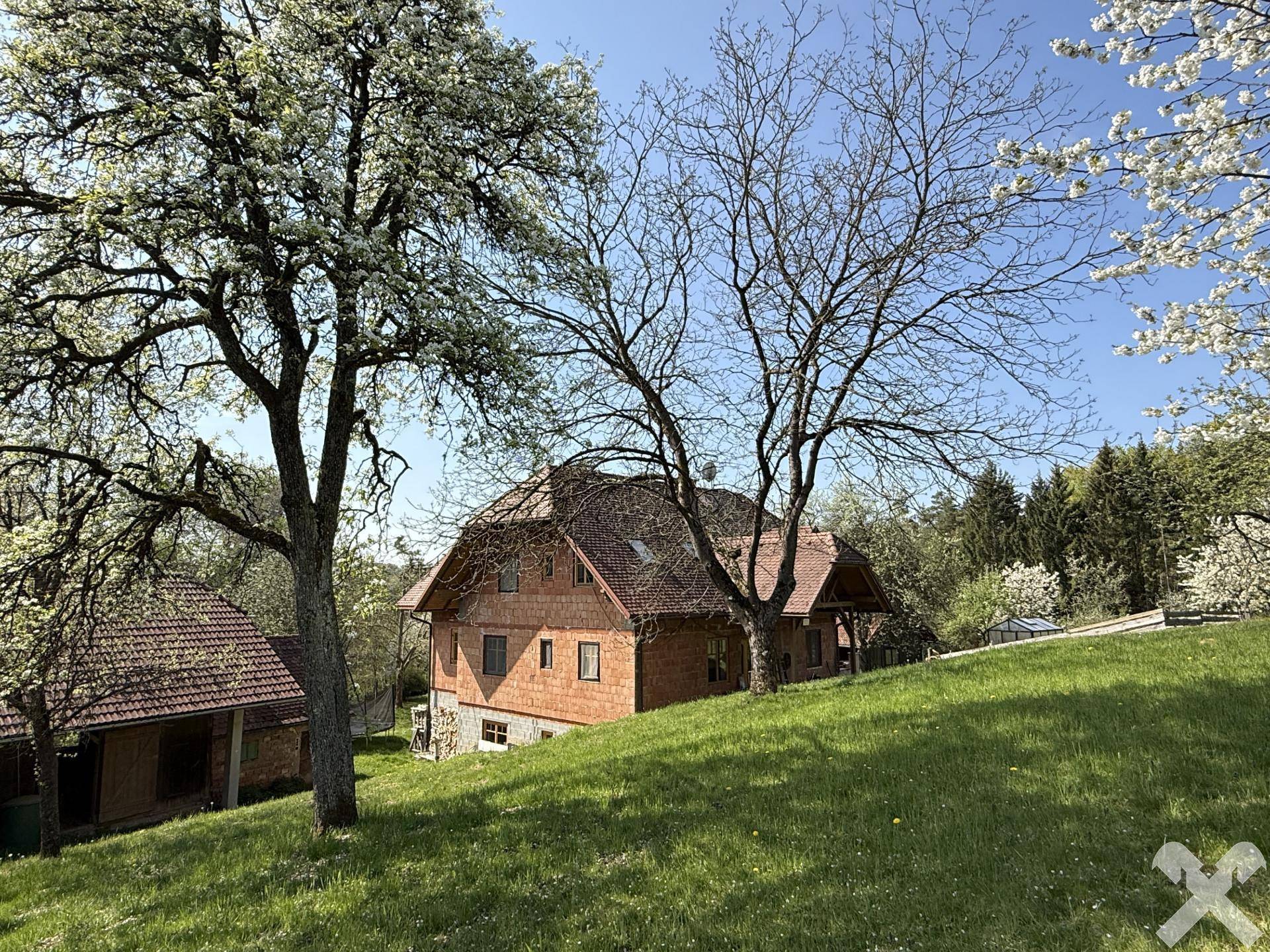 Hauptgebäude aus Holz mit rotem Ziegeldach, umgeben von blühenden Bäumen und grünen Wiesen.