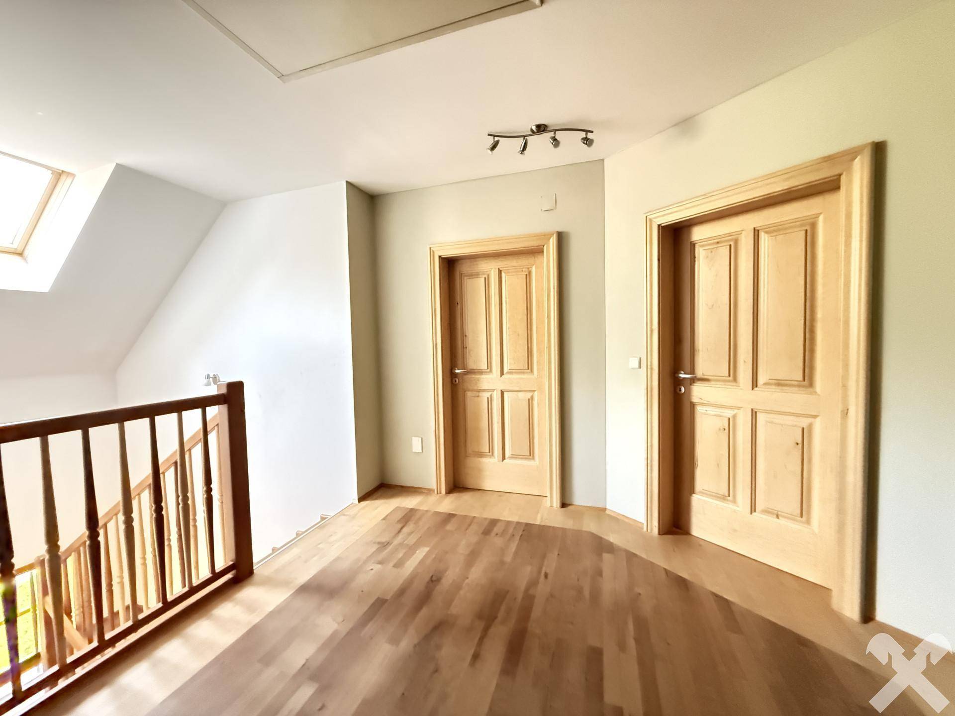 Heller Flur im Obergeschoss mit Holzboden, Holztüren und einem Dachfenster für natürliches Licht.
