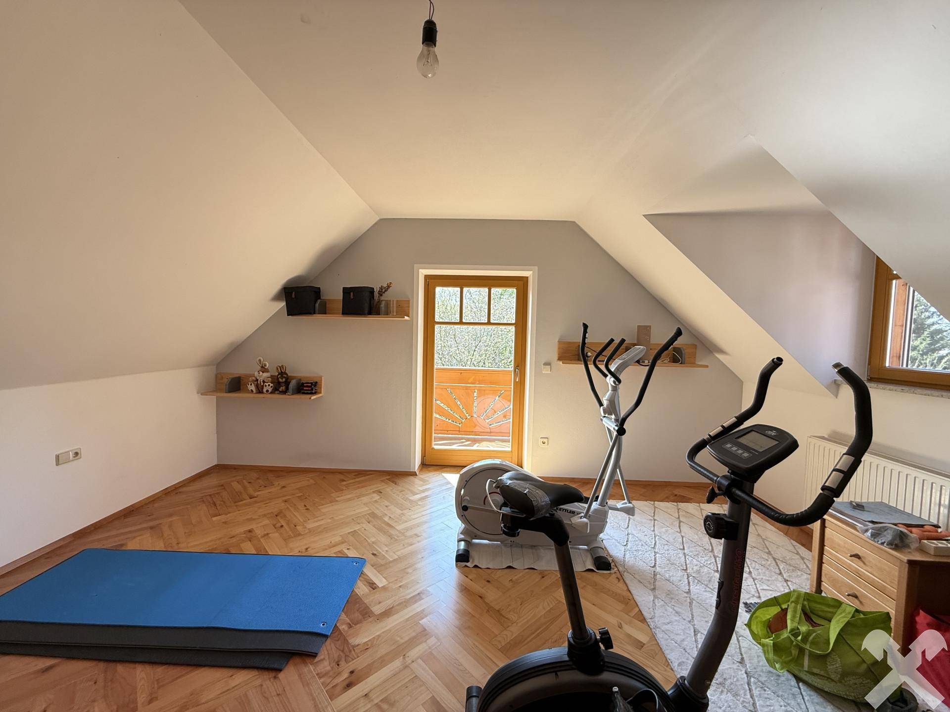 Geräumiger Fitnessraum im Dachgeschoss mit Holzboden, Dachschrägen und Zugang zu einem Balkon.