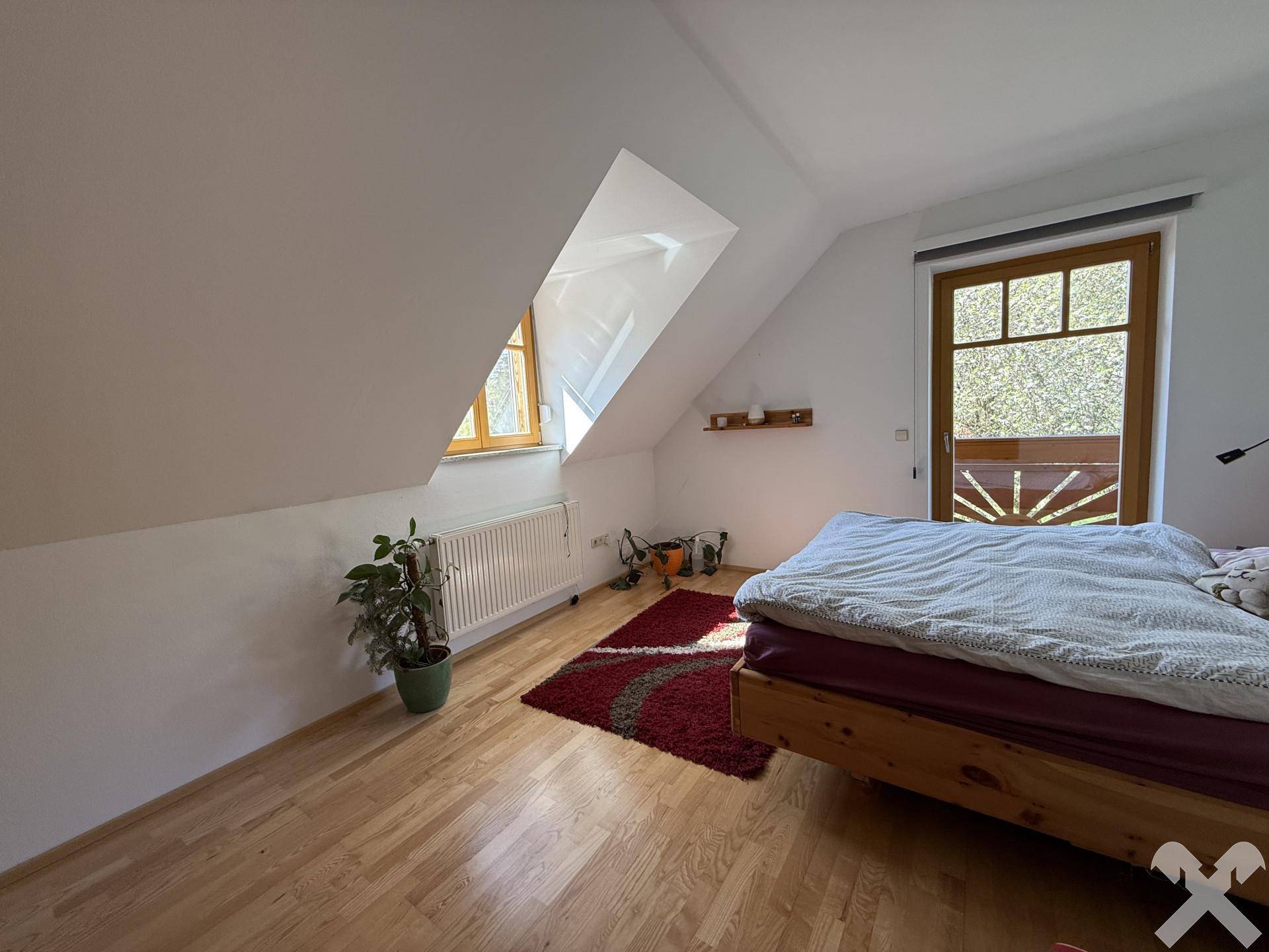 Gemütliches Schlafzimmer im Dachgeschoss mit Holzboden, Dachschrägen und Zugang zu einem Balkon.