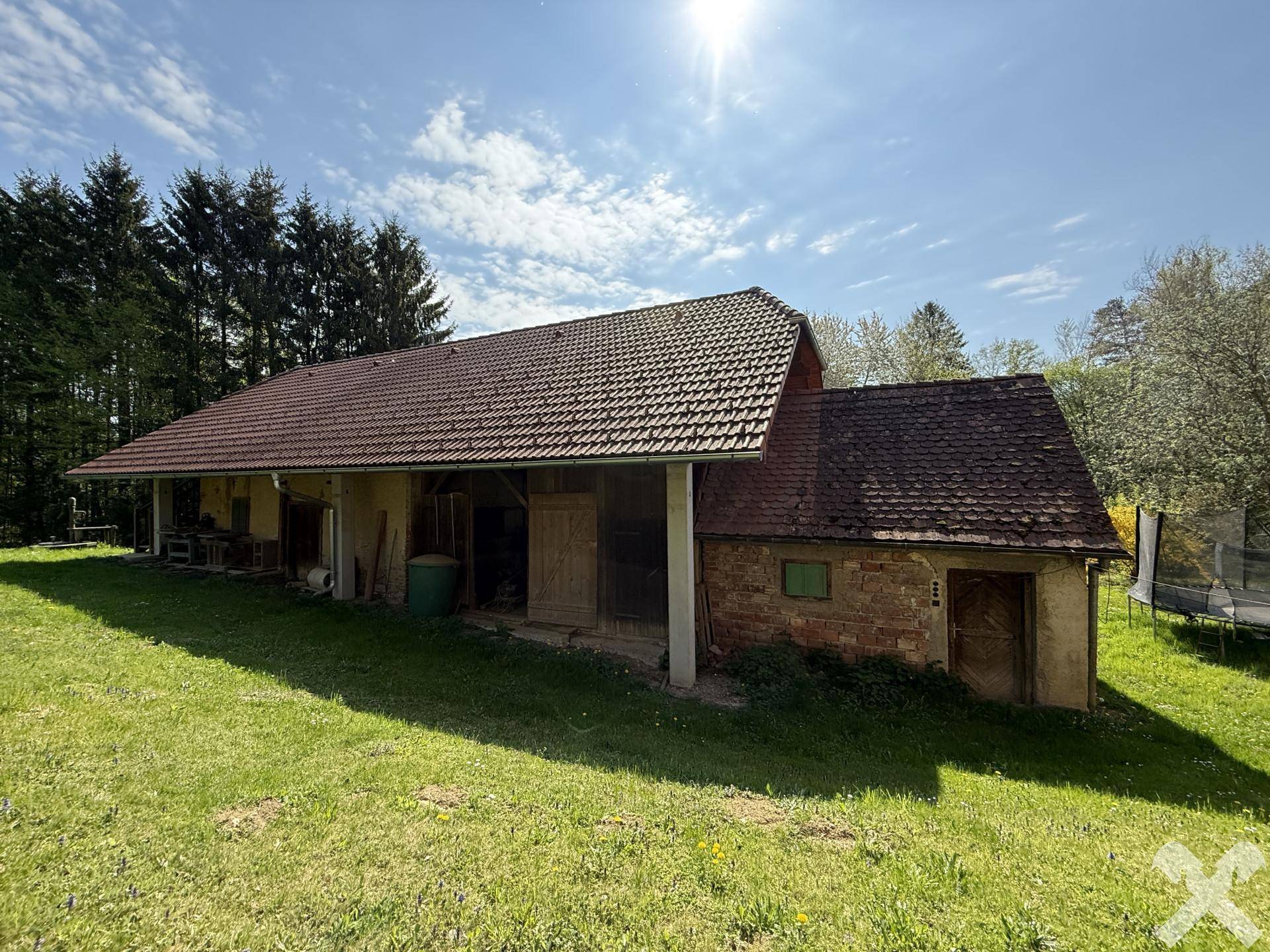 Ländliches Nebengebäude mit Ziegeldach und Holzelementen, umgeben von grüner Wiese.