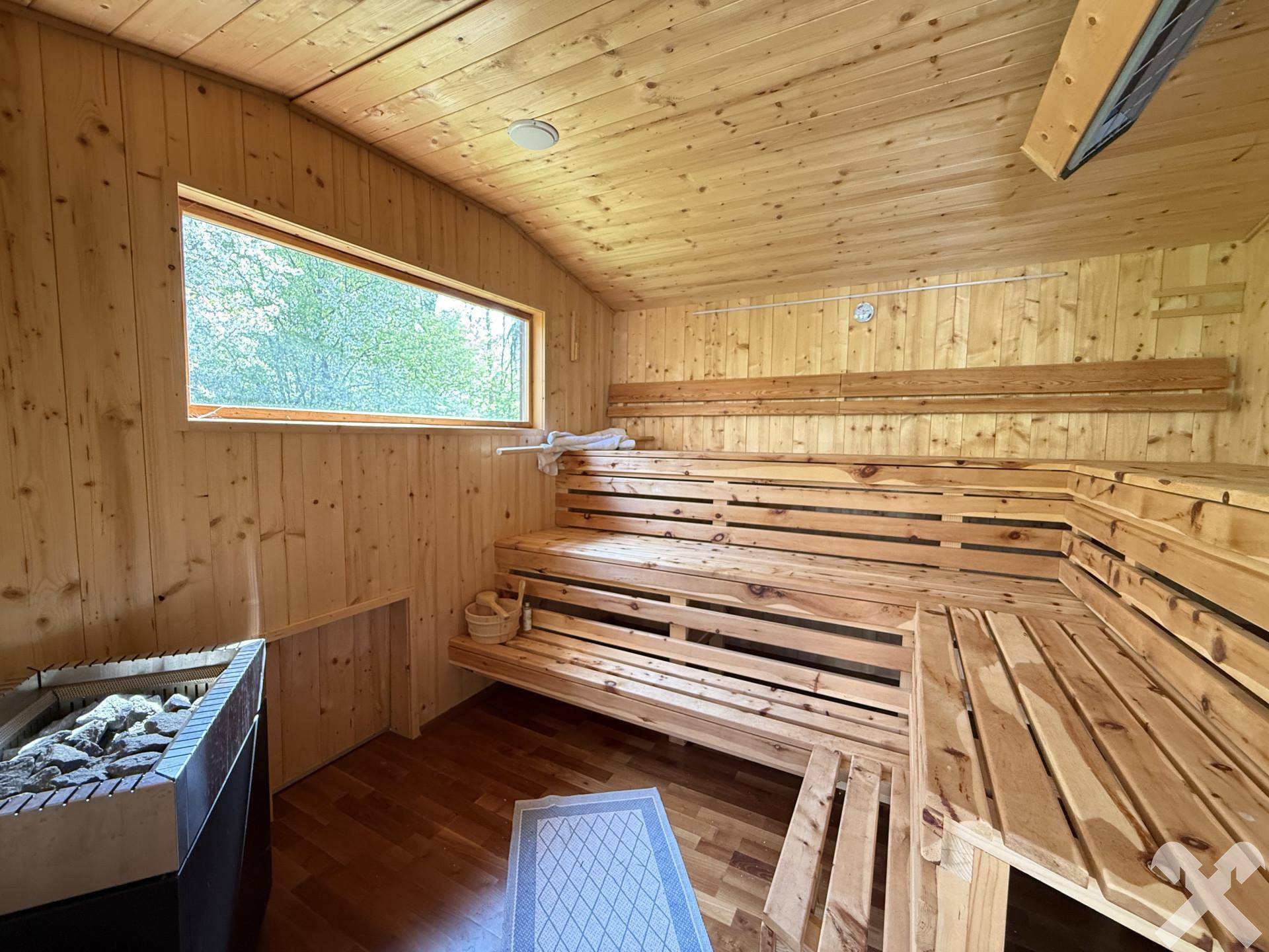 Geräumige Holzsauna mit mehreren Bänken und einem Fenster mit Blick ins Grüne.