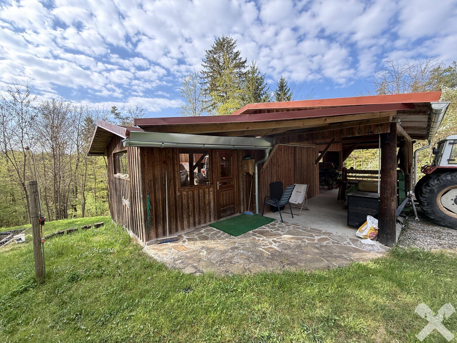Kleine Holzhütte mit überdachtem Terrassenbereich und Sitzgelegenheiten im Grünen.