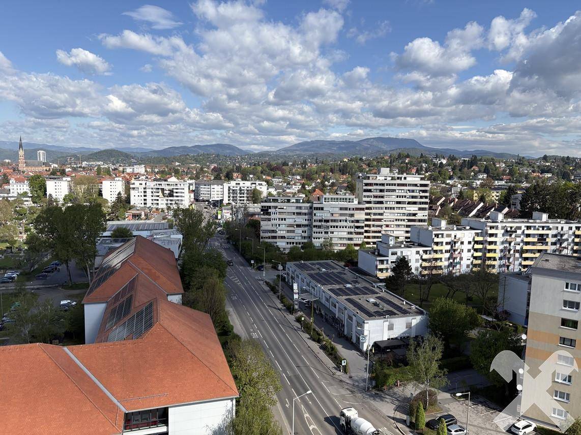 Panoramablick über die Stadt mit Wohngebäuden, Straßen und Bergen im Hintergrund unter blauem Himmel.