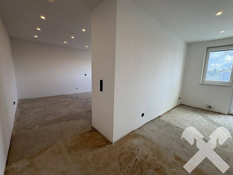 Geräumiger Raum im Rohbau mit großem Fenster und Deckenstrahlern, ideal für individuelle Gestaltung.