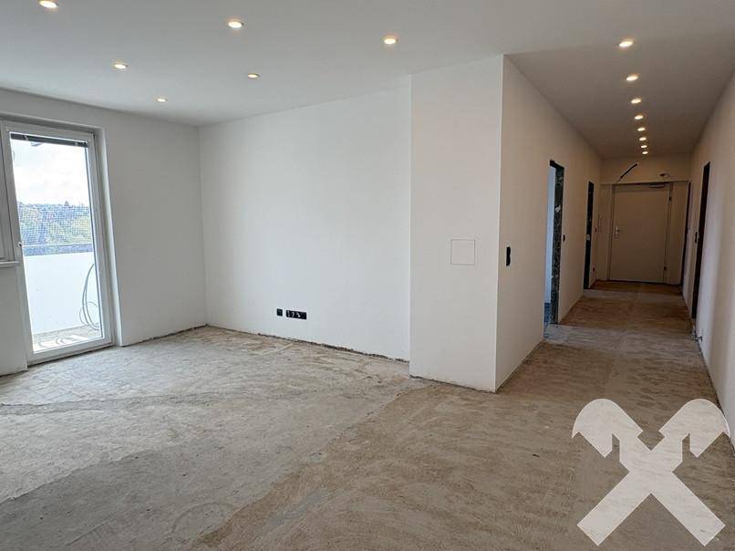 Heller Wohnbereich im Rohbau mit Zugang zum Balkon und Deckenstrahlern, bereit für den Innenausbau.
