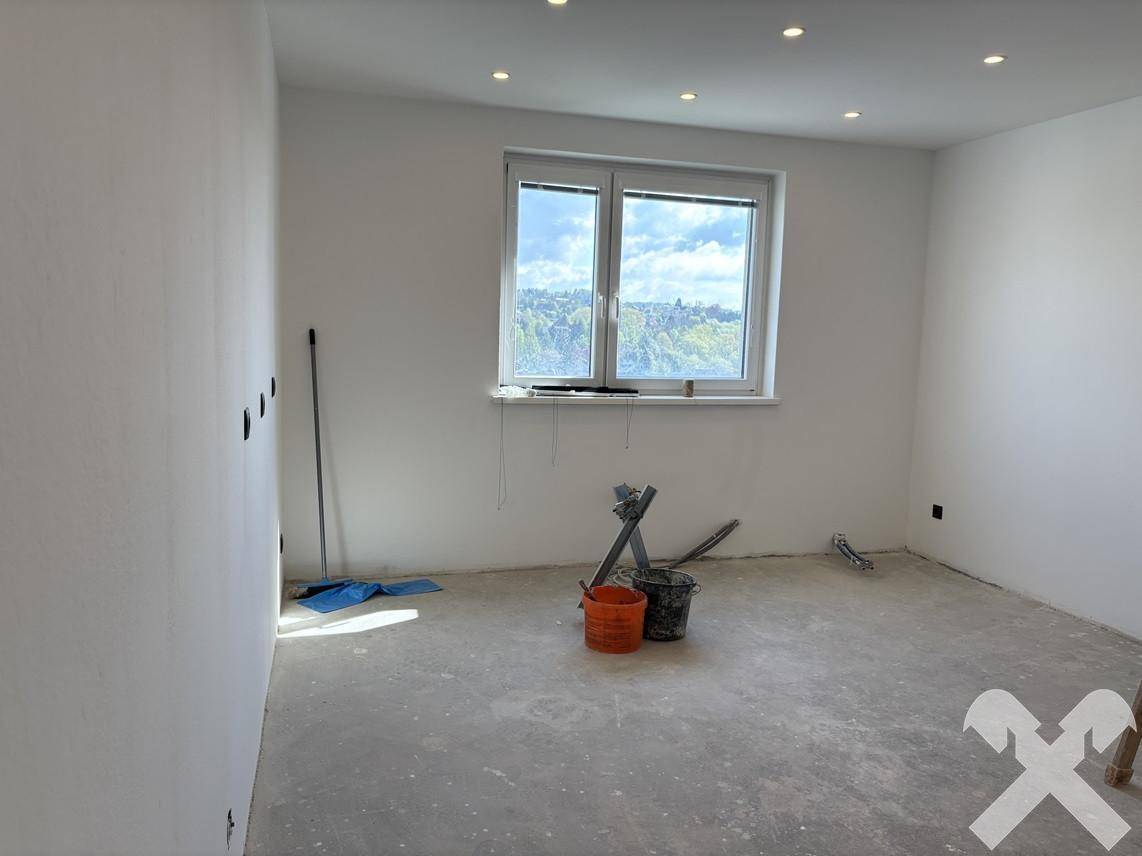 Zimmer im Rohbau mit großem Fenster und Deckenstrahlern, bereit für die individuelle Gestaltung.