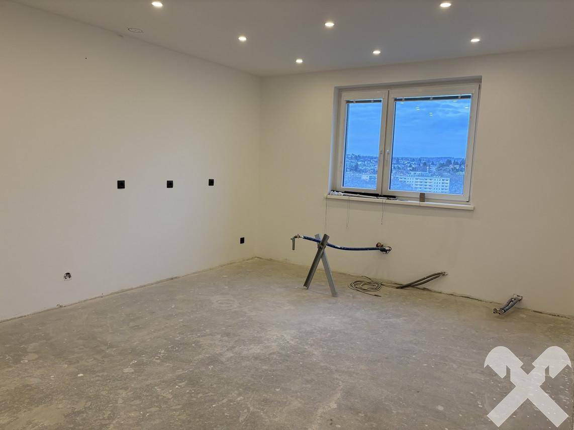 Raum im Rohbau mit vorbereiteten Anschlüssen für eine Küche und großem Fenster.