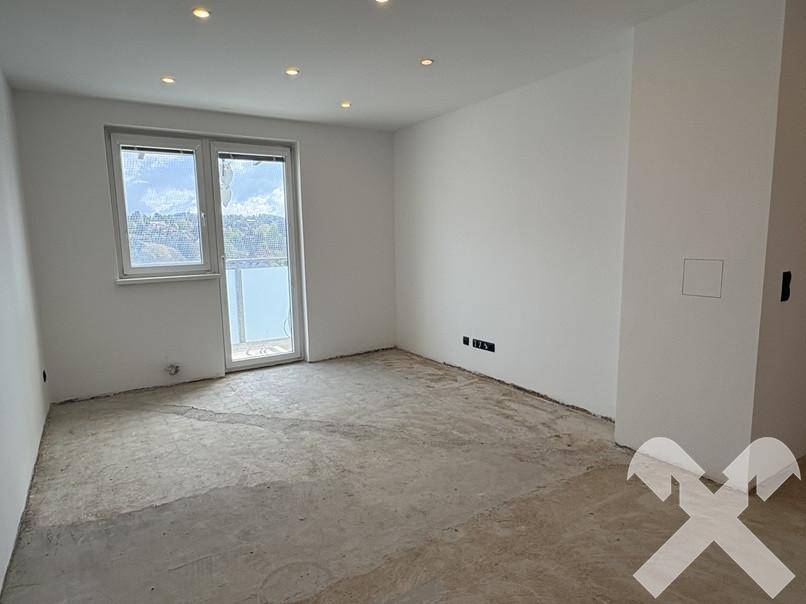 Heller Wohnraum im Rohbau mit großem Fenster und Balkonzugang, bereit für die Fertigstellung.
