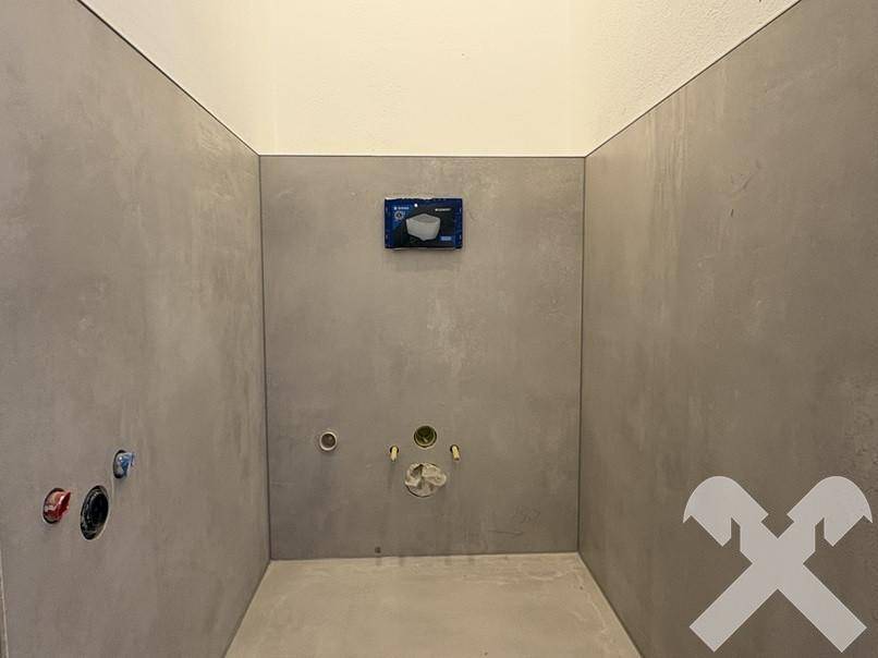 WC-Raum im Rohbau mit grauen Fliesen und vorbereiteter Installation für die Wandtoilette.