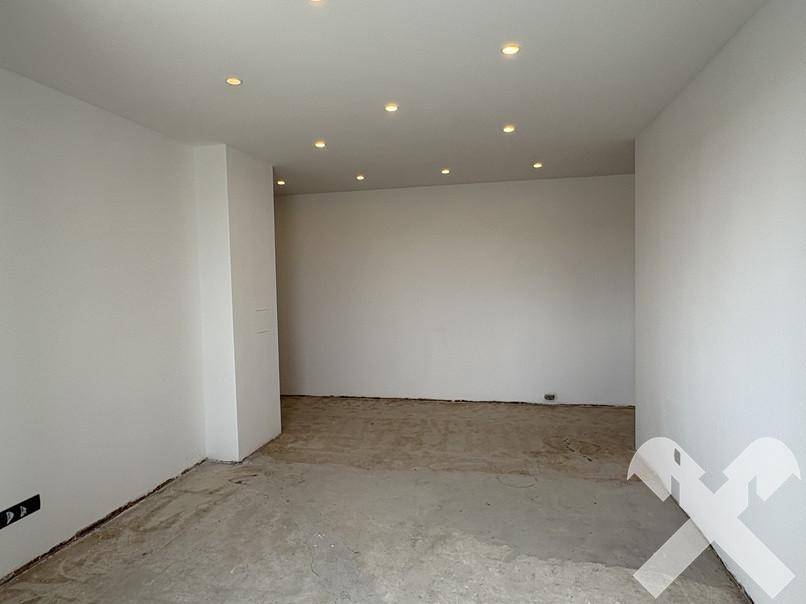 Leerer Raum im Rohbau mit Deckenstrahlern und weiß gestrichenen Wänden, wartet auf den Ausbau.