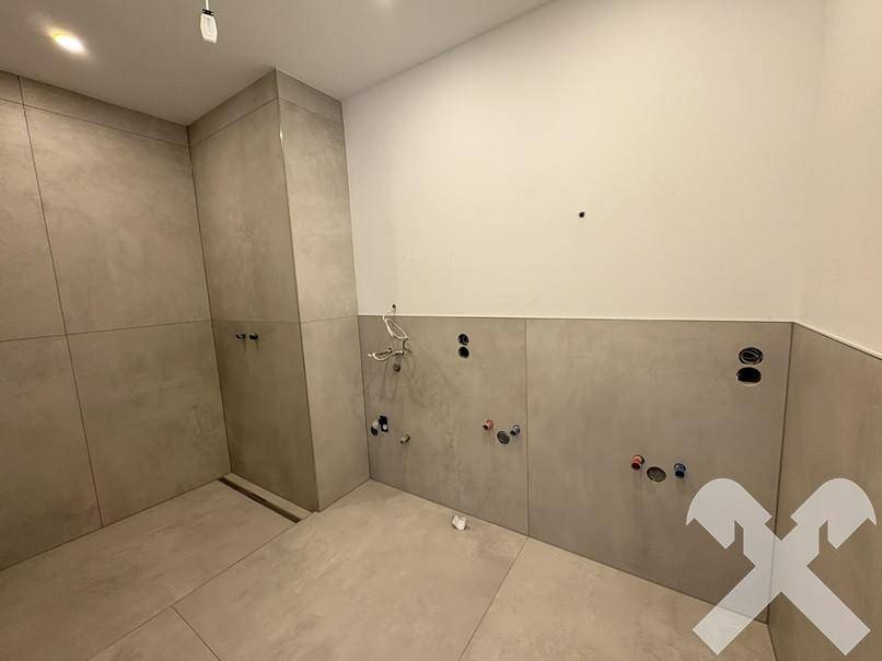 Modernes Badezimmer im Rohbau mit großformatigen Fliesen und vorbereiteten Anschlüssen für Dusche und Waschtisch.