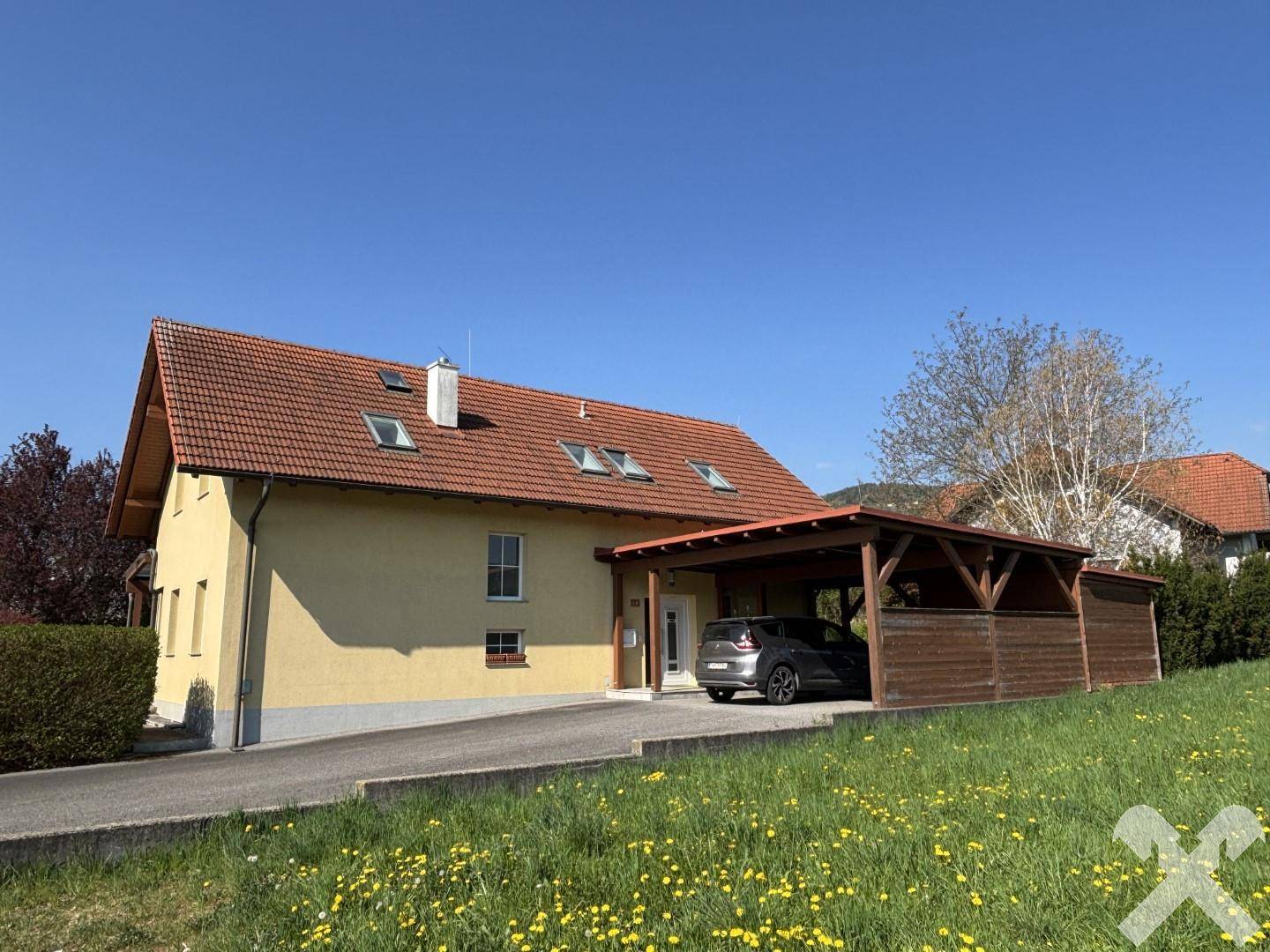 Vorderansicht des Hauses mit Carport, Einfahrt und gepflegtem Vorgarten.