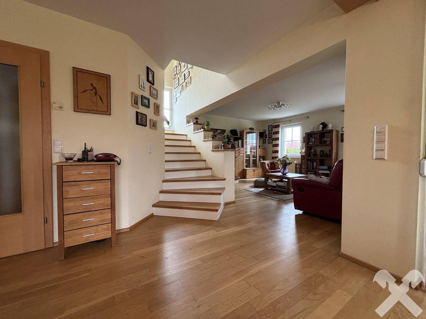 Heller Eingangsbereich mit Holztreppe und Zugang zum offenen Wohnzimmer.
