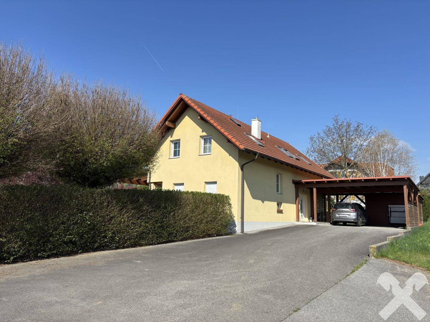 Hauszufahrt mit Carport und Hecke, die das Grundstück von der Straße abgrenzt.