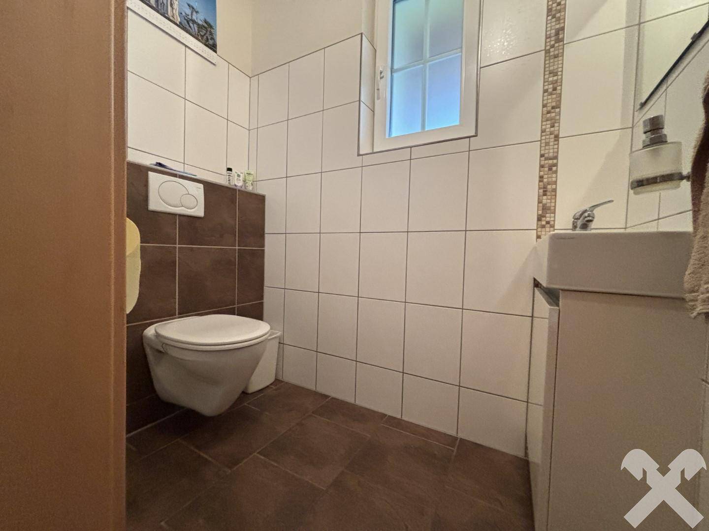 Modern gefliestes Gäste-WC mit wandhängendem WC und kleinem Waschbecken.