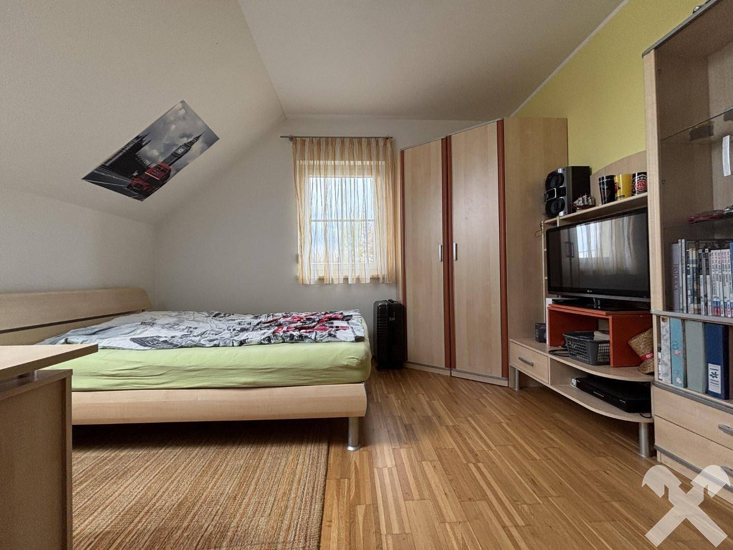 Schlafzimmer mit Holzboden, Kleiderschrank und Fenster mit Blick ins Freie.