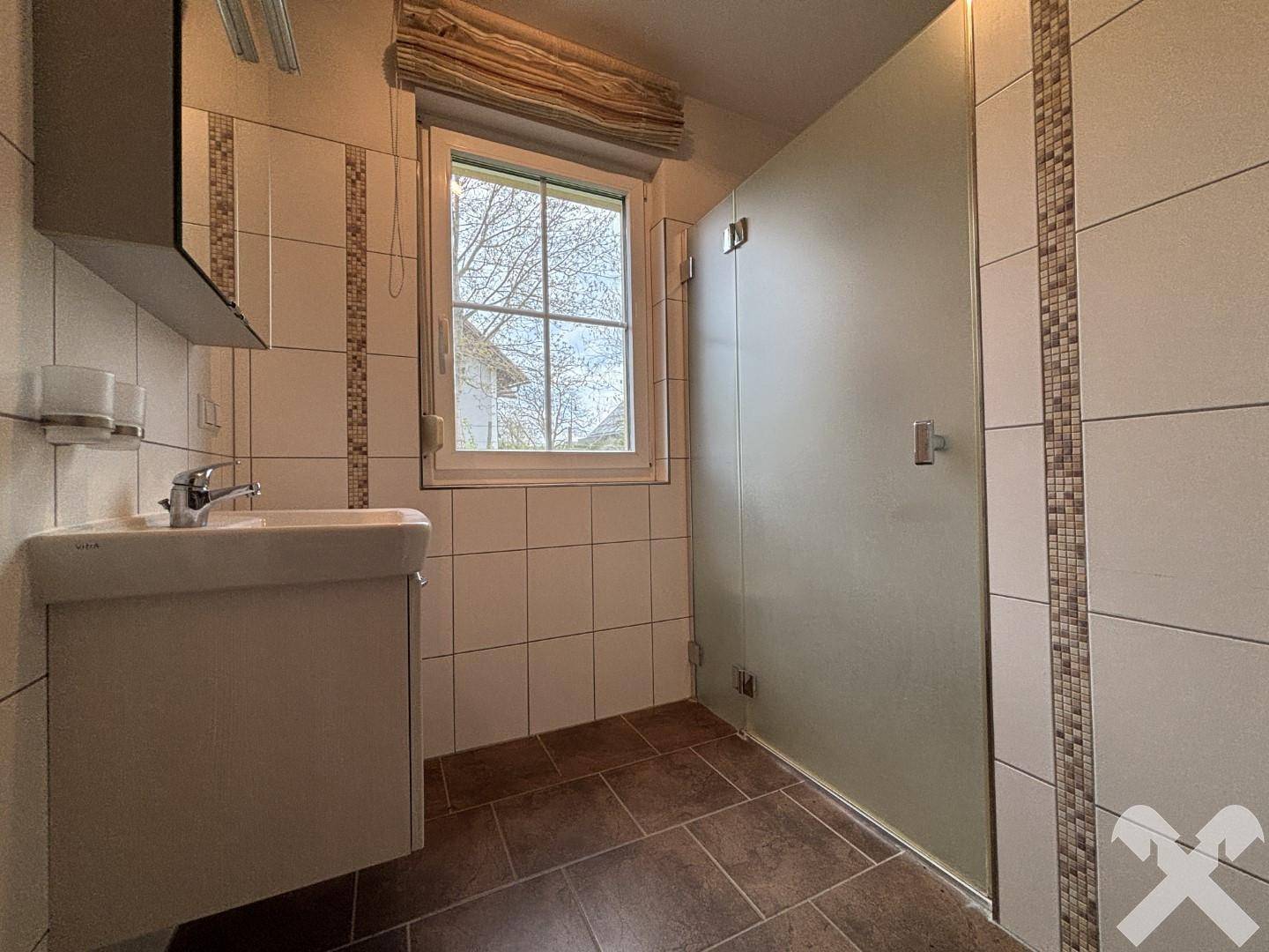 Modernes Badezimmer mit Dusche, Waschbecken und Fenster für natürliche Belüftung.