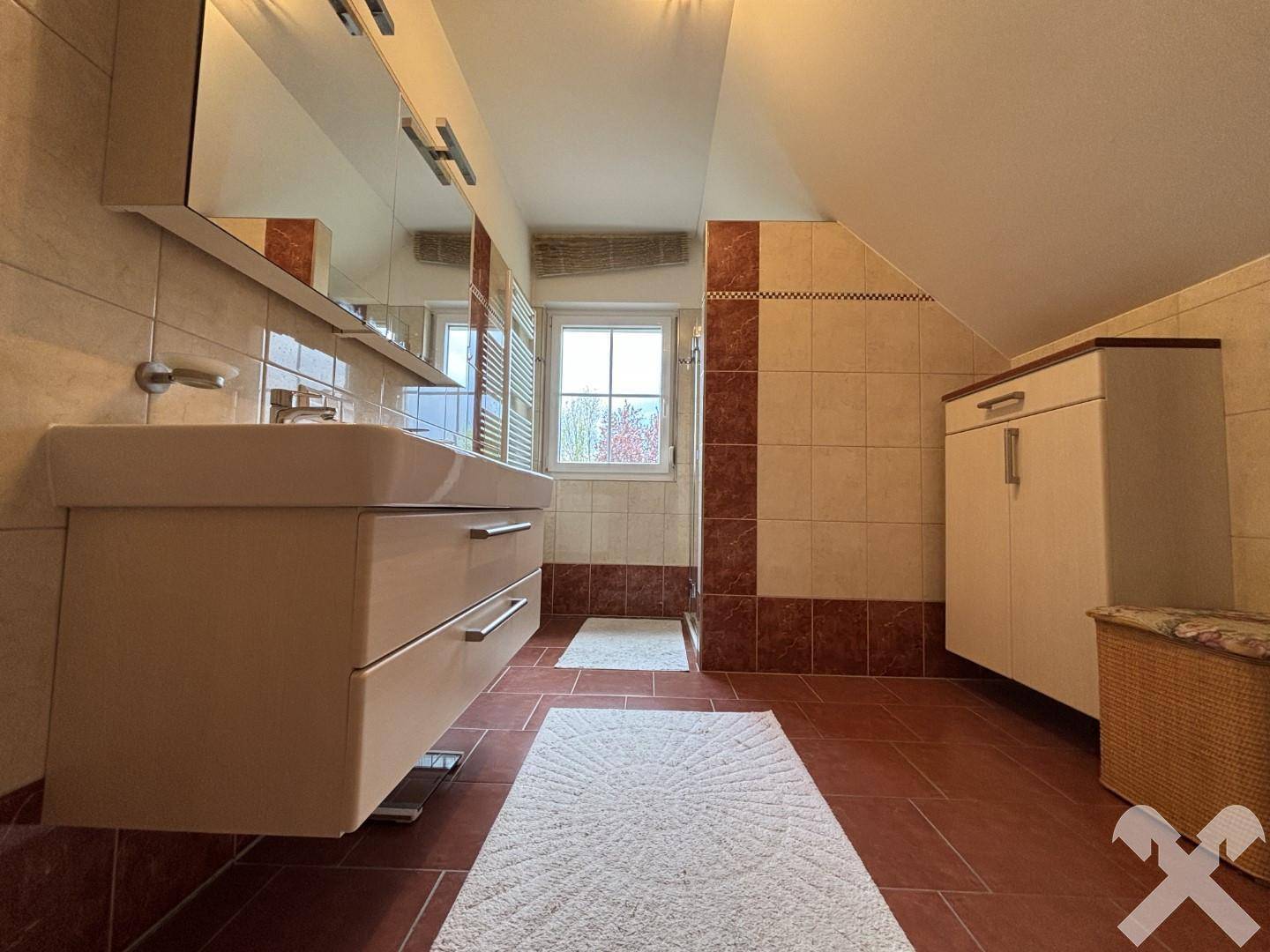 Helles Badezimmer mit Doppelwaschbecken, Spiegelschrank und Fenster.