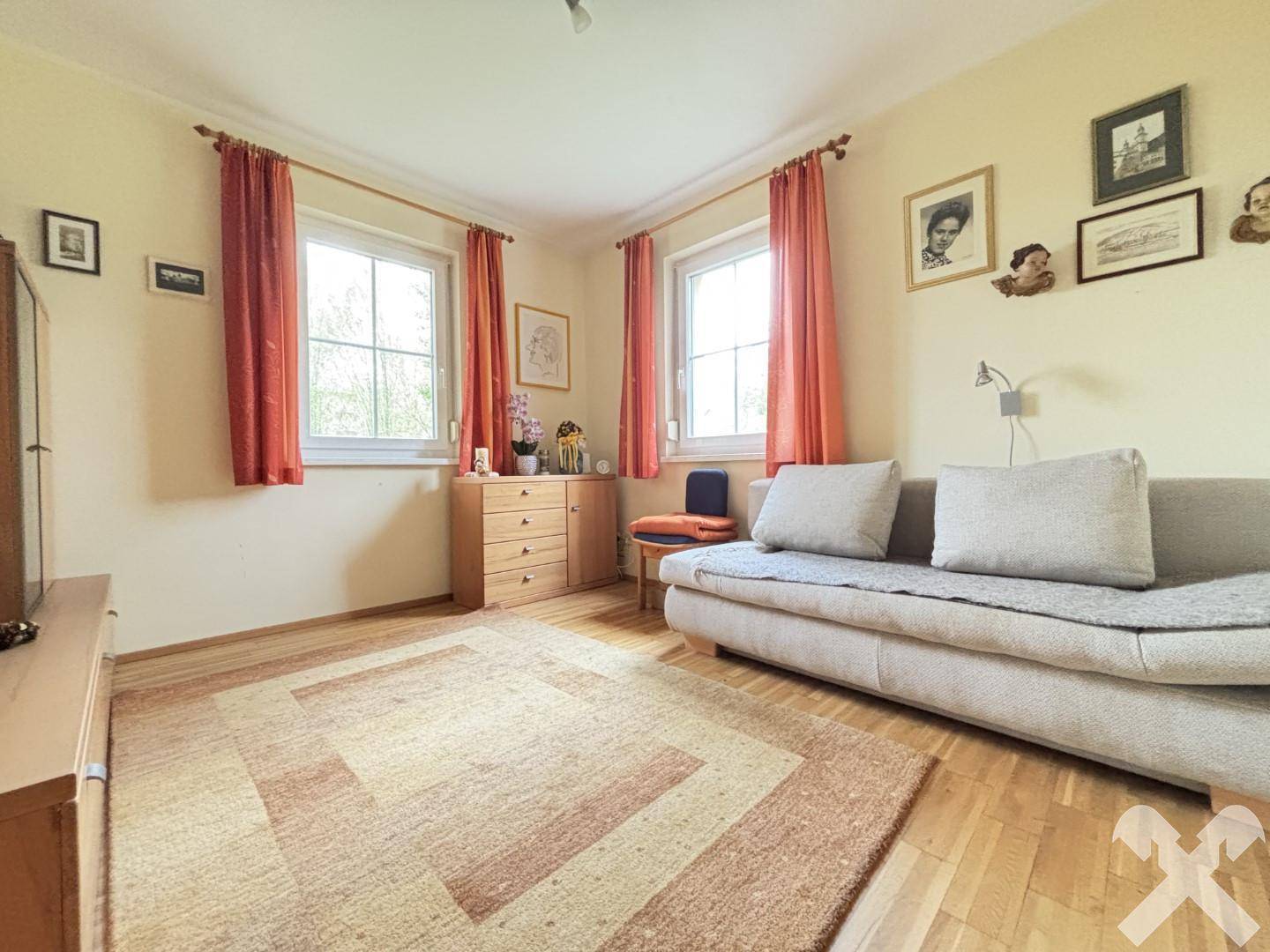 Helles Schlafzimmer mit Holzboden, bequemer Couch und Fenstern mit Blick ins Grüne.