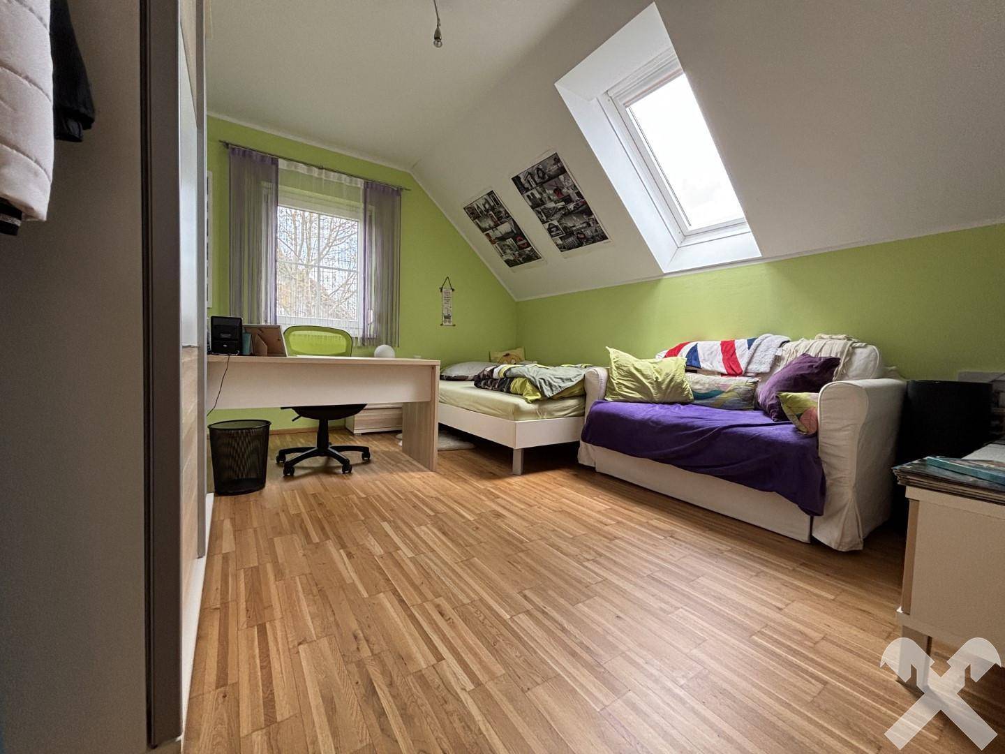 Kinderzimmer mit Holzboden, Schreibtisch, Bett und Dachfenster für viel Licht.