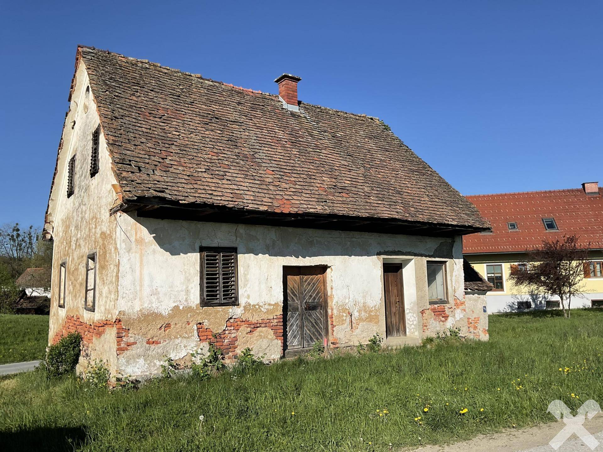 Nahaufnahme der verwitterten Fassade des alten Hauses mit bröckelndem Putz und Holztüren.