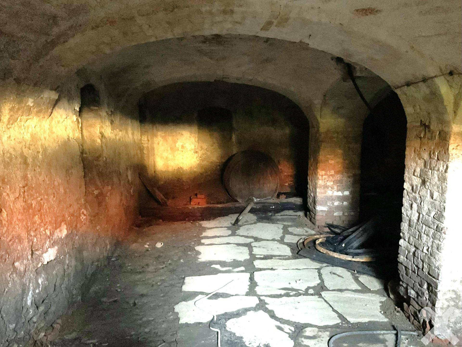 Historischer Gewölbekeller mit Ziegelwänden, Steinboden und einem großen Holzfass.