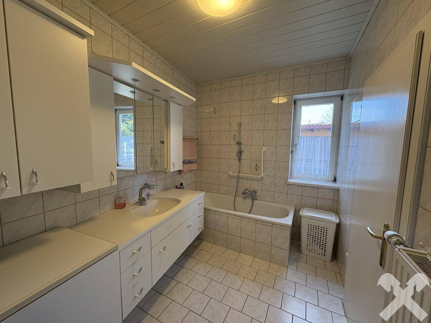 Gefliestes Badezimmer mit Badewanne, Doppelwaschbecken und Fenster für Tageslicht und Belüftung.