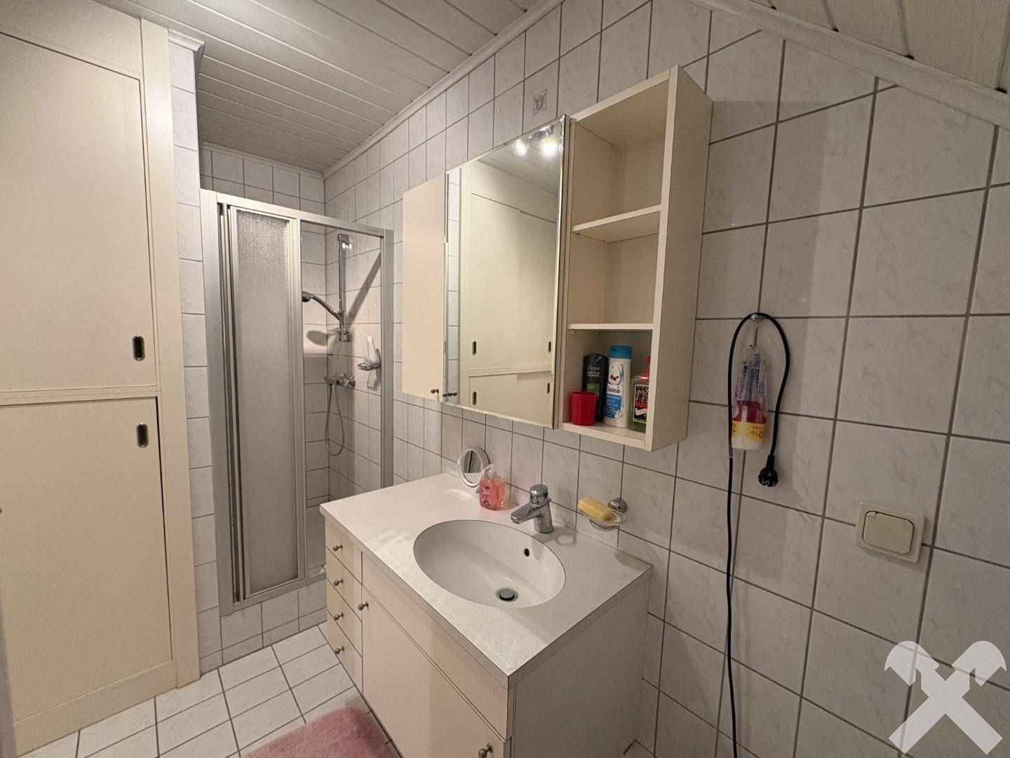 Kleines Badezimmer mit Duschkabine, Waschbecken und Spiegelschrank für den täglichen Bedarf.